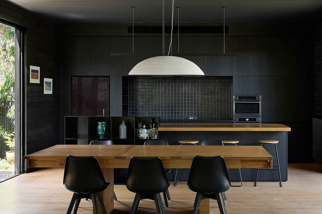 Modern, minimalist kitchen with dark walls, wooden table, and pendant lamp.