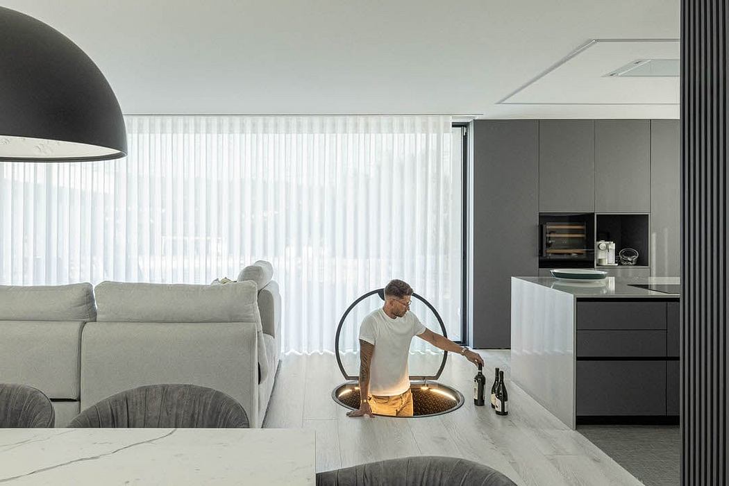 Minimalist, open-plan living space with sleek kitchen and suspended lighting fixture.