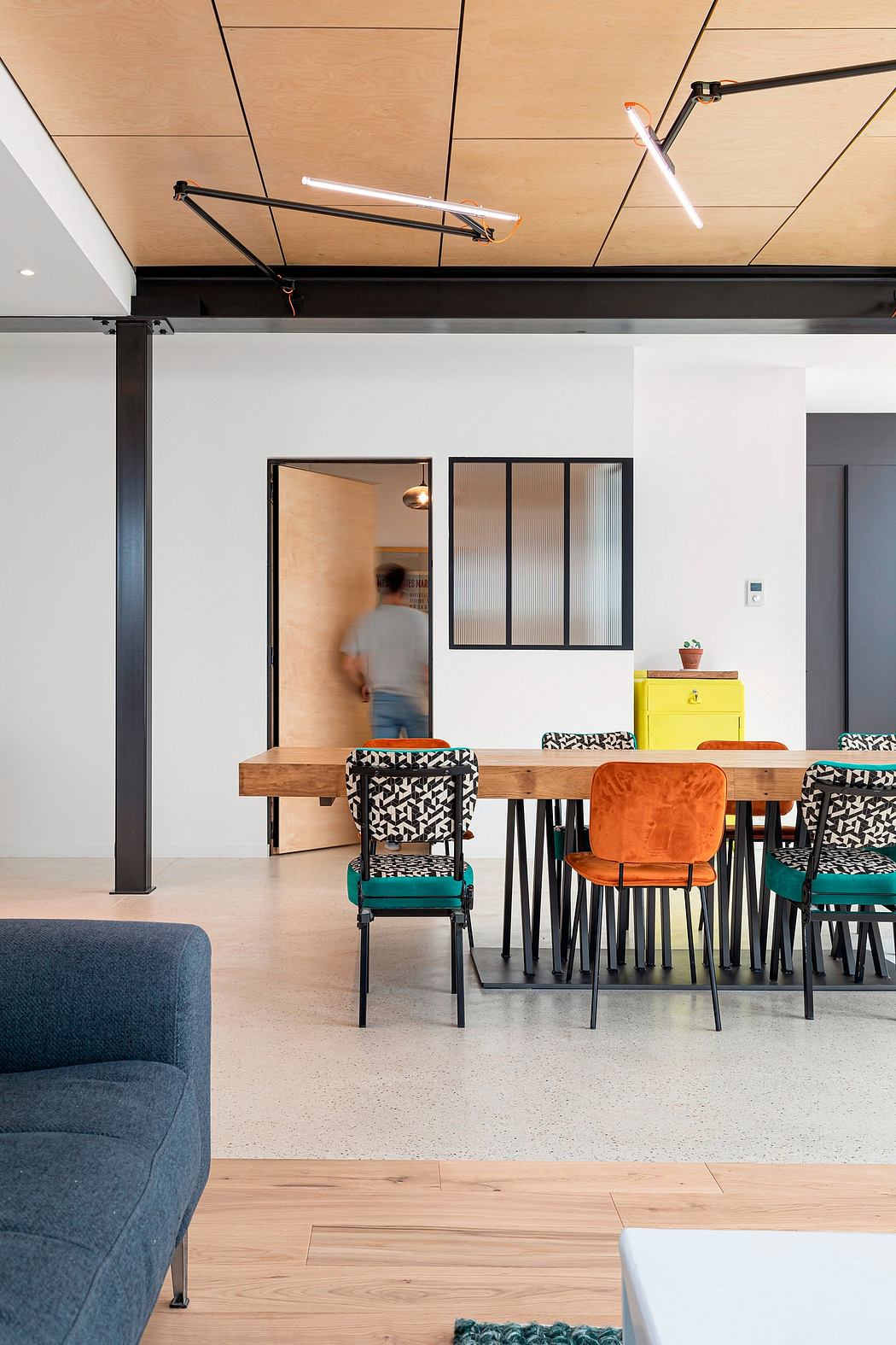 Vibrant, eclectic home office with wooden desks, patterned chairs, and modern lighting.