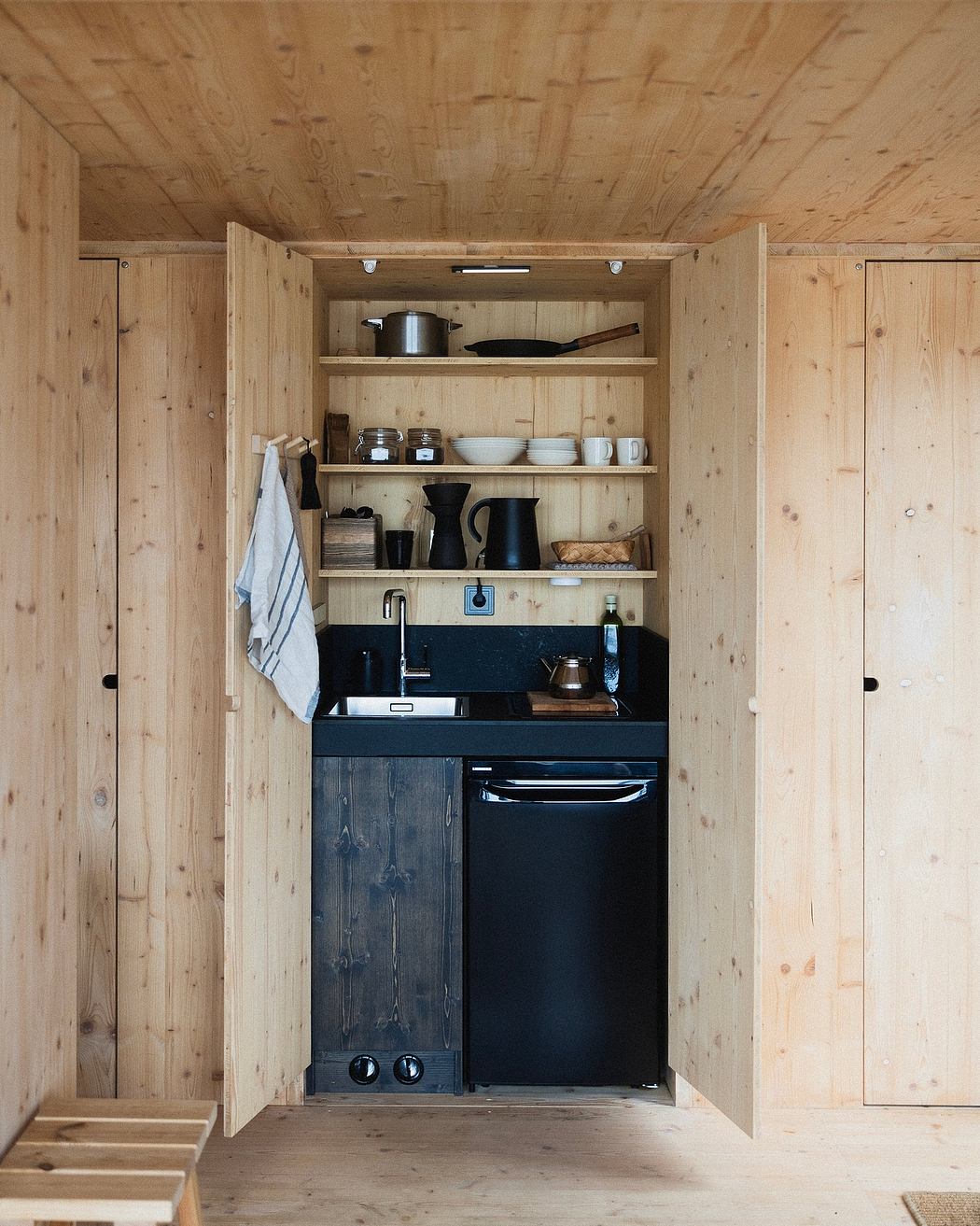A cozy cabin kitchen with a compact design, wooden walls, and ample shelving.