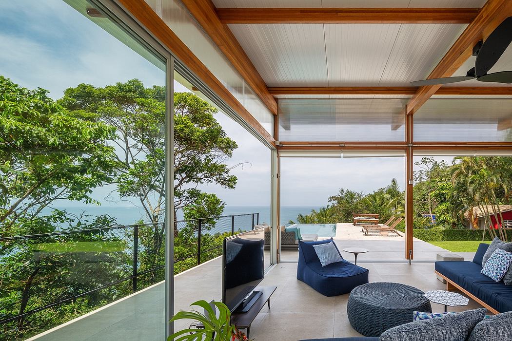 Modern tropical home with expansive glass walls, wood ceiling beams, and plush seating.