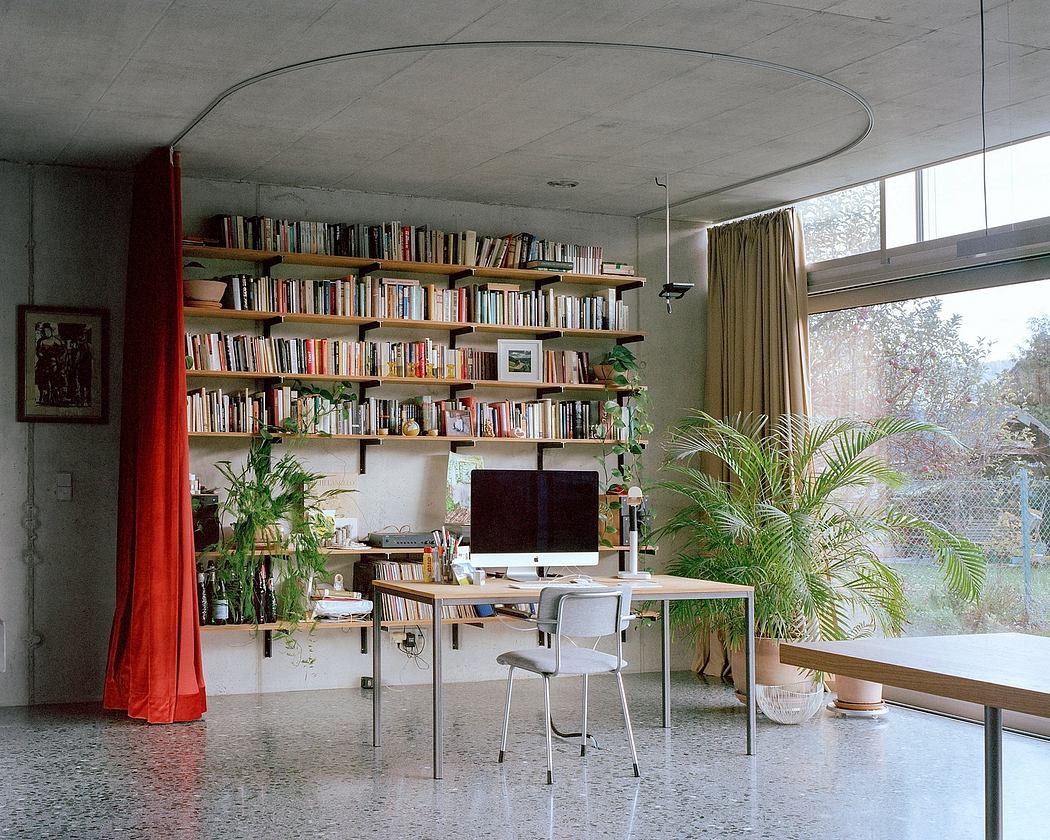 Cozy home office nook with built-in bookshelves, plants, and large windows overlooking nature.