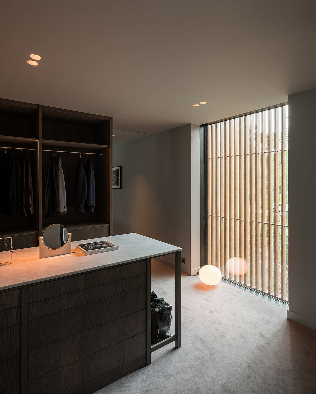 A modern, minimalist bedroom with a built-in wardrobe, vanity, and large floor-to-ceiling windows.