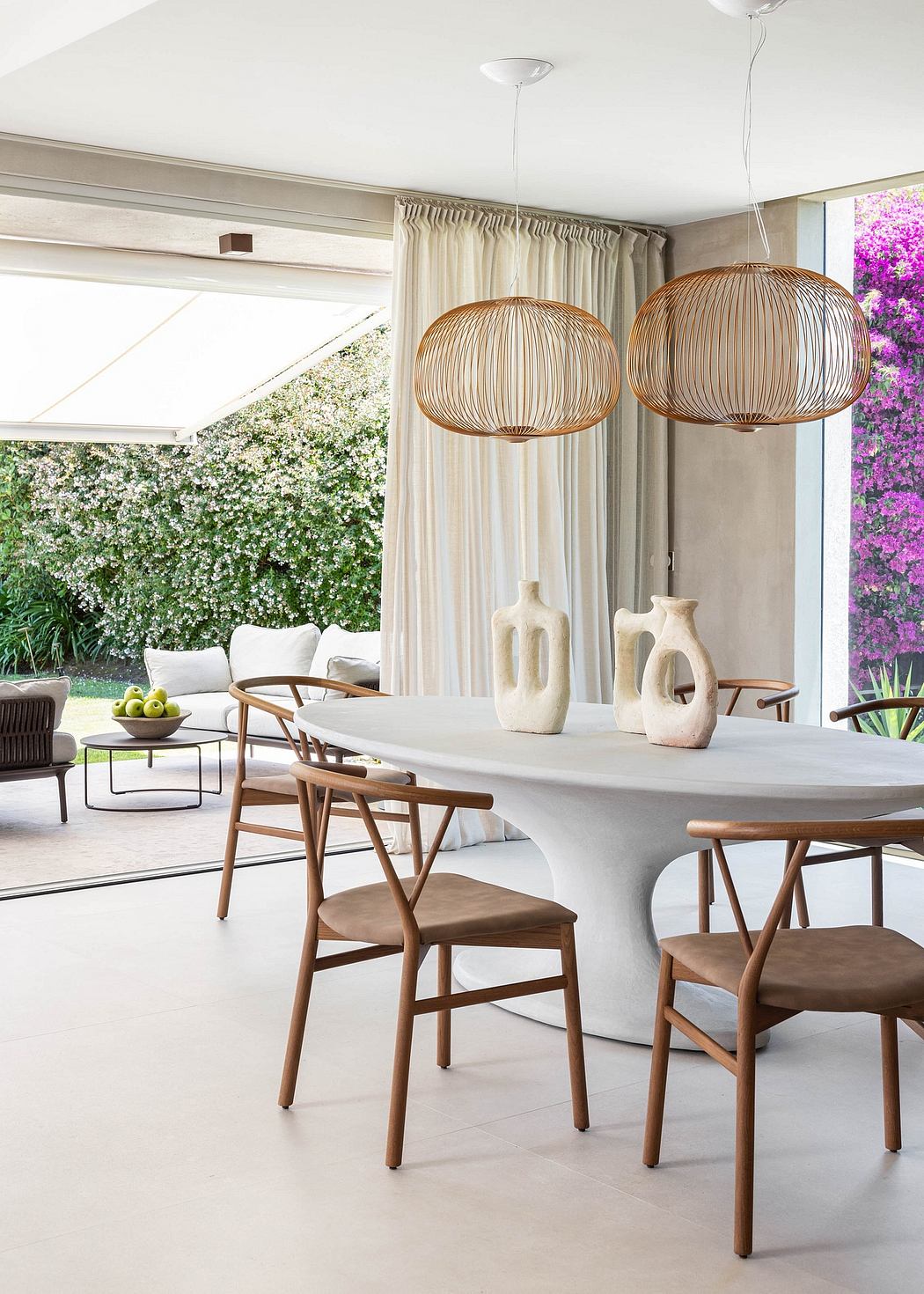 Modern dining area with natural wood furniture, pendant lights, and lush outdoor view.