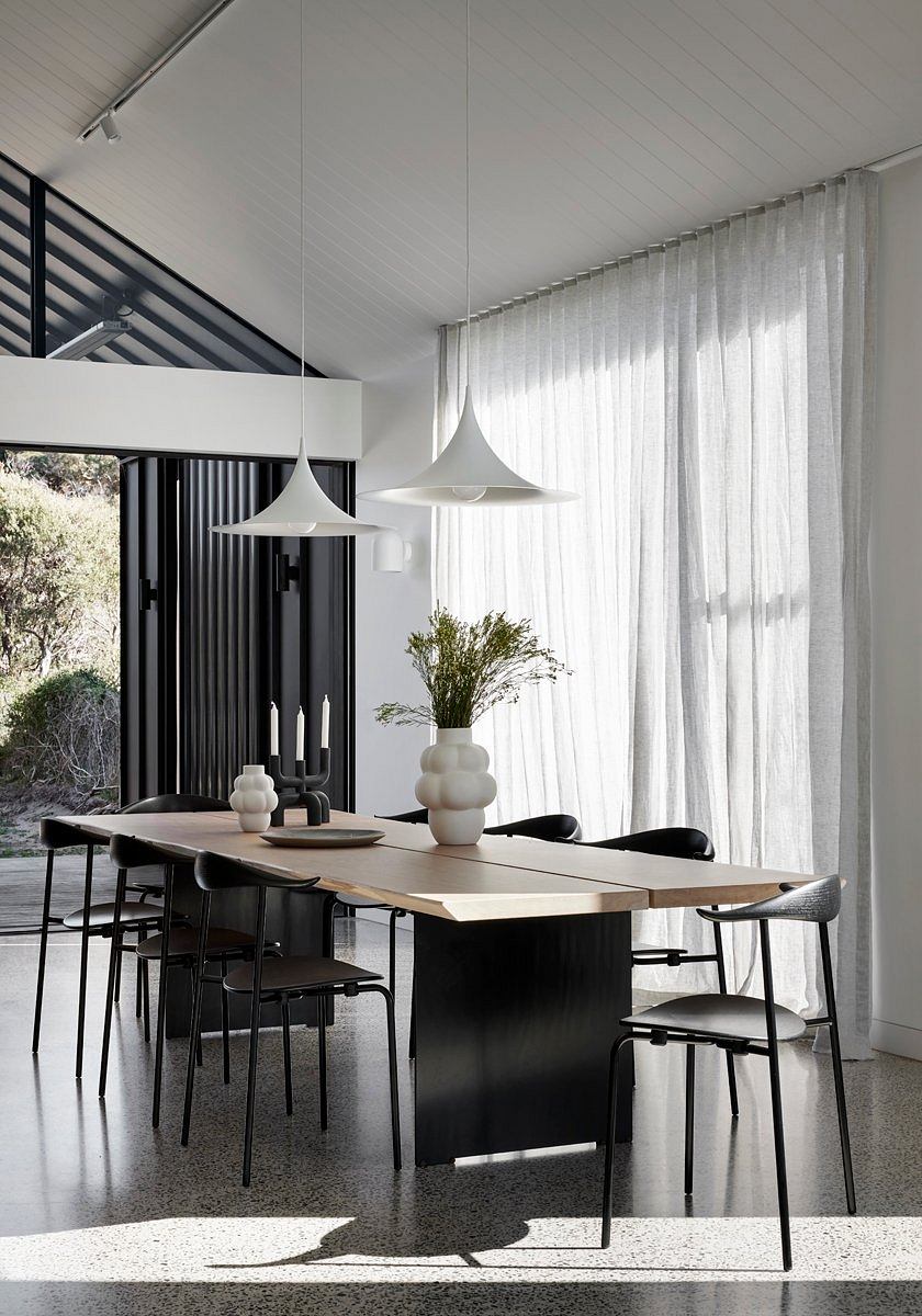 Modern dining space with high-ceilinged architecture, minimal pendant lamps, and timbered table.