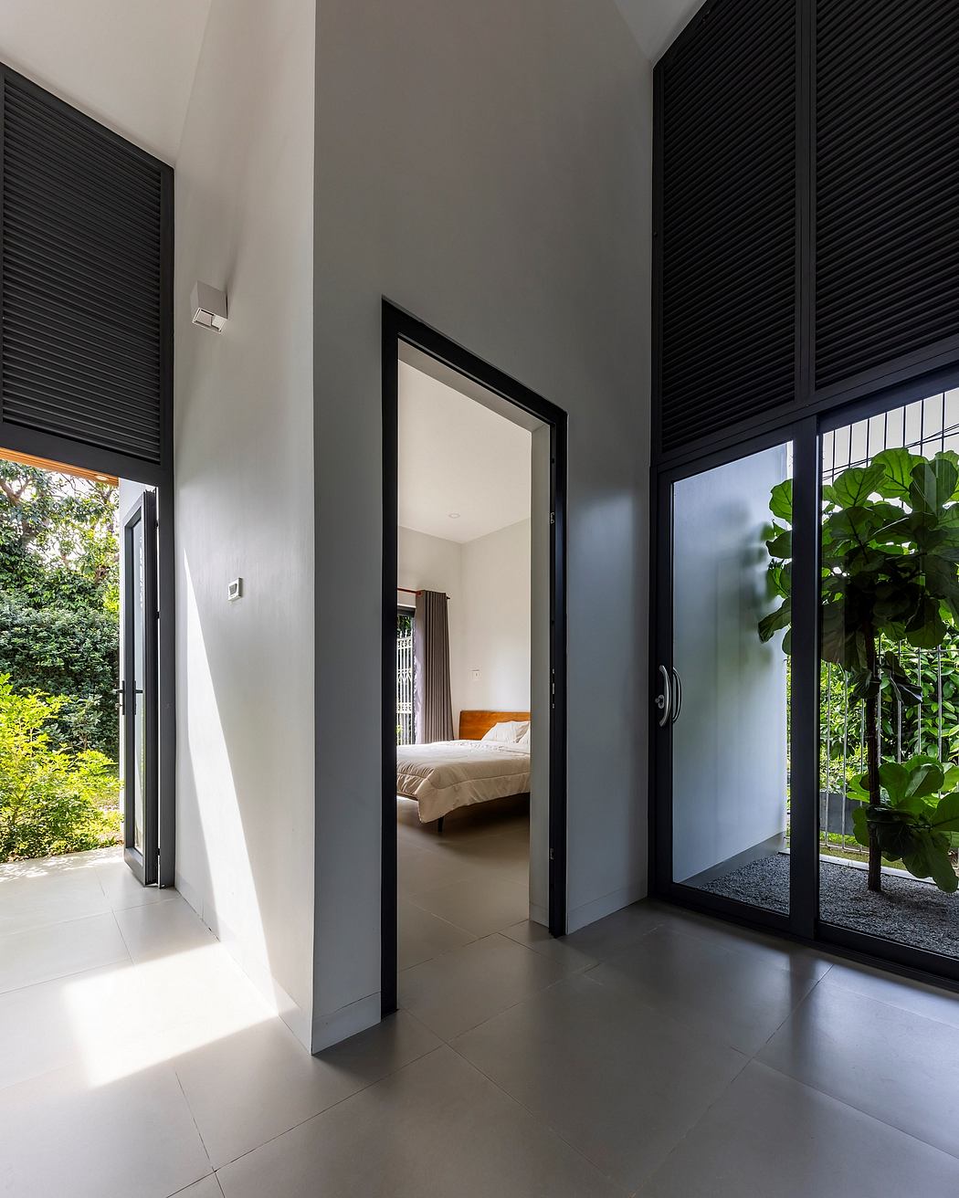 Modern architectural interior with black window shutters, large windows, and lush greenery outside.
