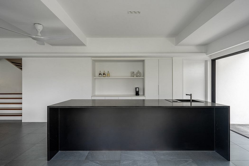 Sleek, minimalist kitchen with a large black island and open shelving in a bright, modern space.