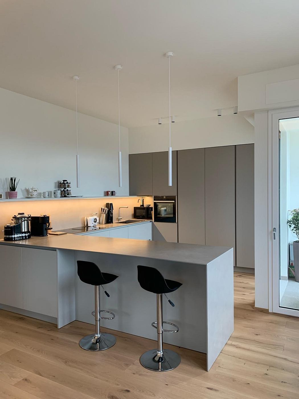 A modern, minimalist kitchen with a sleek island, pendant lighting, and hardwood floors.