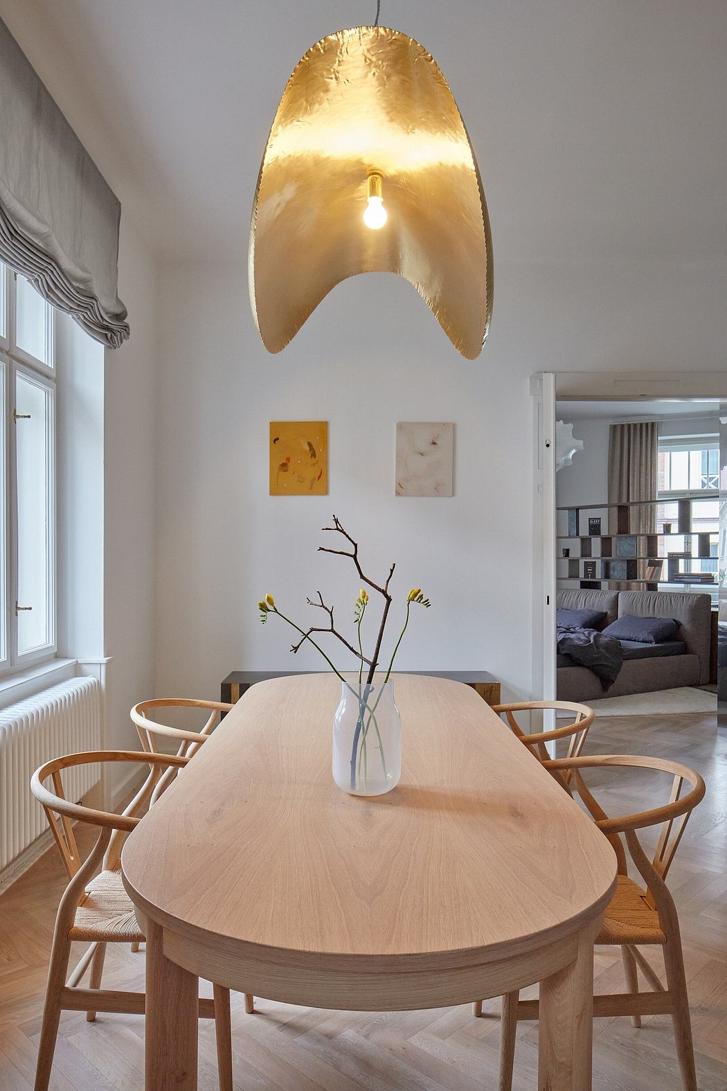 A contemporary dining space with a golden-hued, sculptural pendant light and wooden furniture.