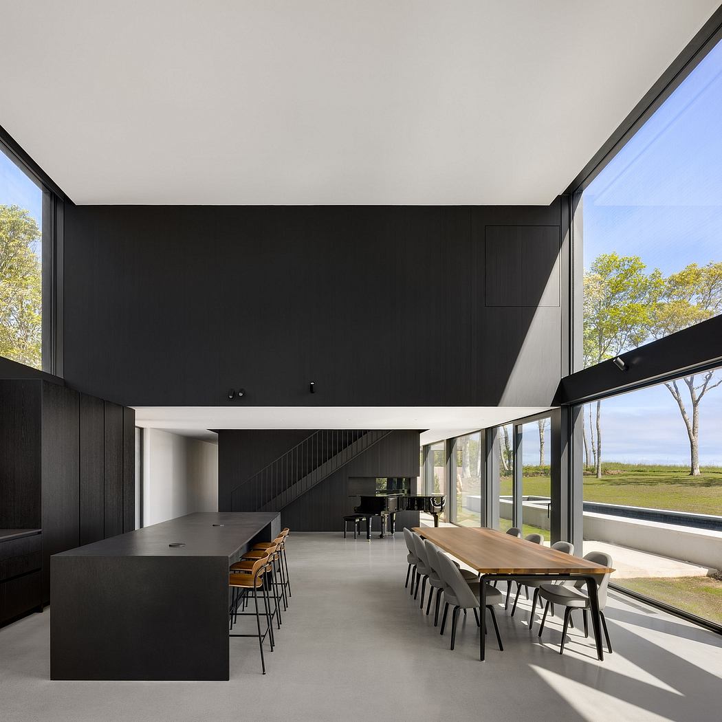 Expansive black and gray interior with a wooden dining table, modern kitchen, and views of the outdoors.