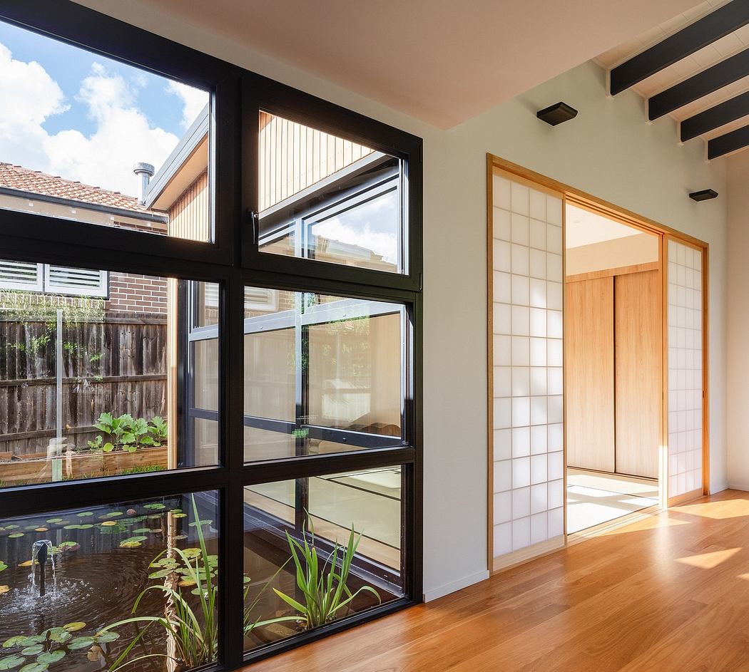 A modern interior with large windows, wooden floors, and a tranquil indoor pond.