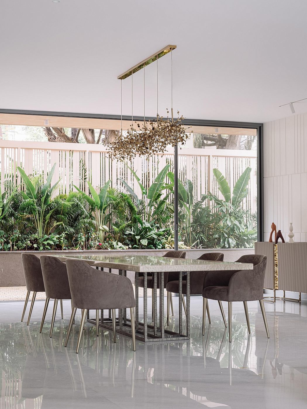 Sleek modern dining room with glass walls, tropical plants, and a chandelier.