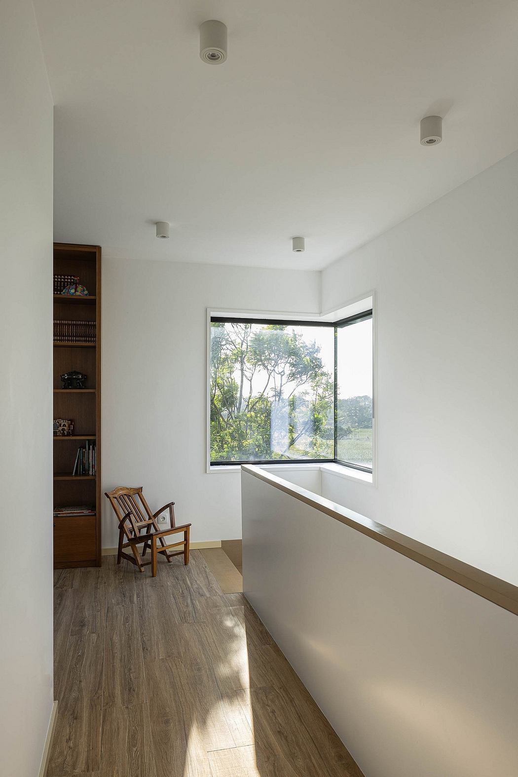 Minimalist interior with large window framing lush greenery outside, wooden shelves, and armchairs.