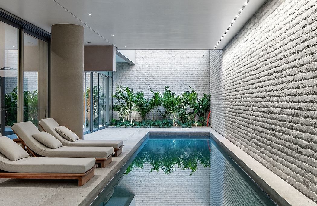 Sleek minimalist indoor pool area with textured concrete wall, glass windows, and comfortable lounge chairs.