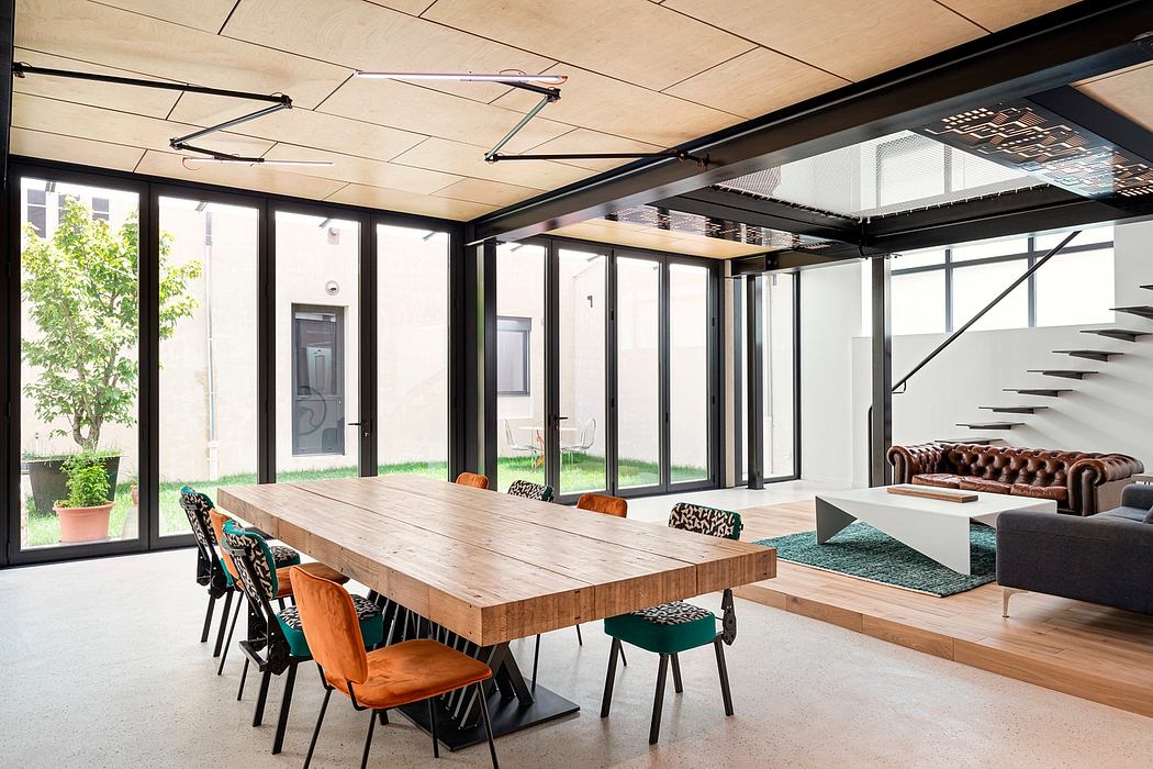 Spacious open-concept interior with a large wooden dining table, plush seating, and floor-to-ceiling windows overlooking a lush outdoor space.