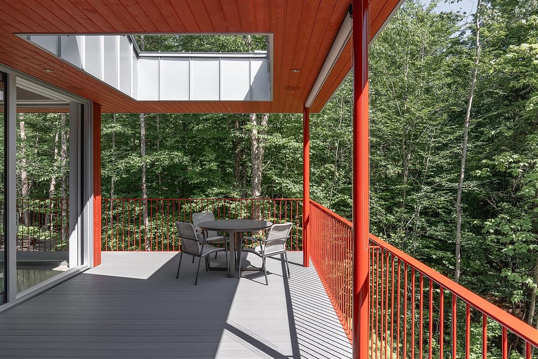 Striking modern cabin with vibrant orange exterior, expansive deck, and forested backdrop.