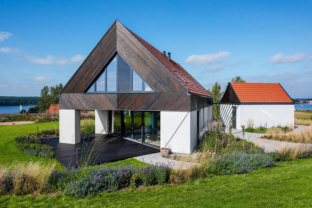 Modern A-frame home with large windows, red roof, and well-landscaped garden.