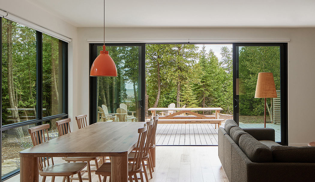Contemporary open-plan living space with wooden furnishings, expansive glass windows, and outdoor deck.