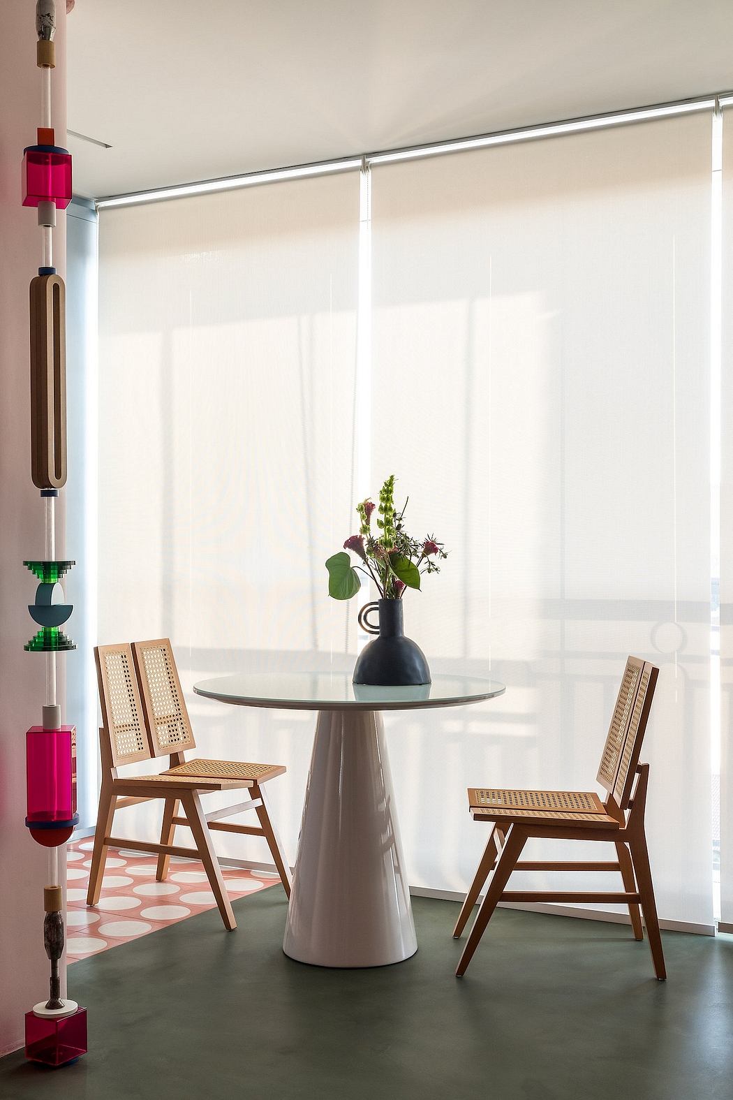 Modern, minimalist interior with geometric table, cane chairs, and potted plants.