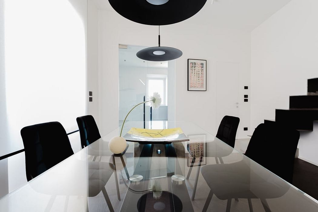 Modern minimalist dining room with glass table, black chairs, and angular lighting fixture.