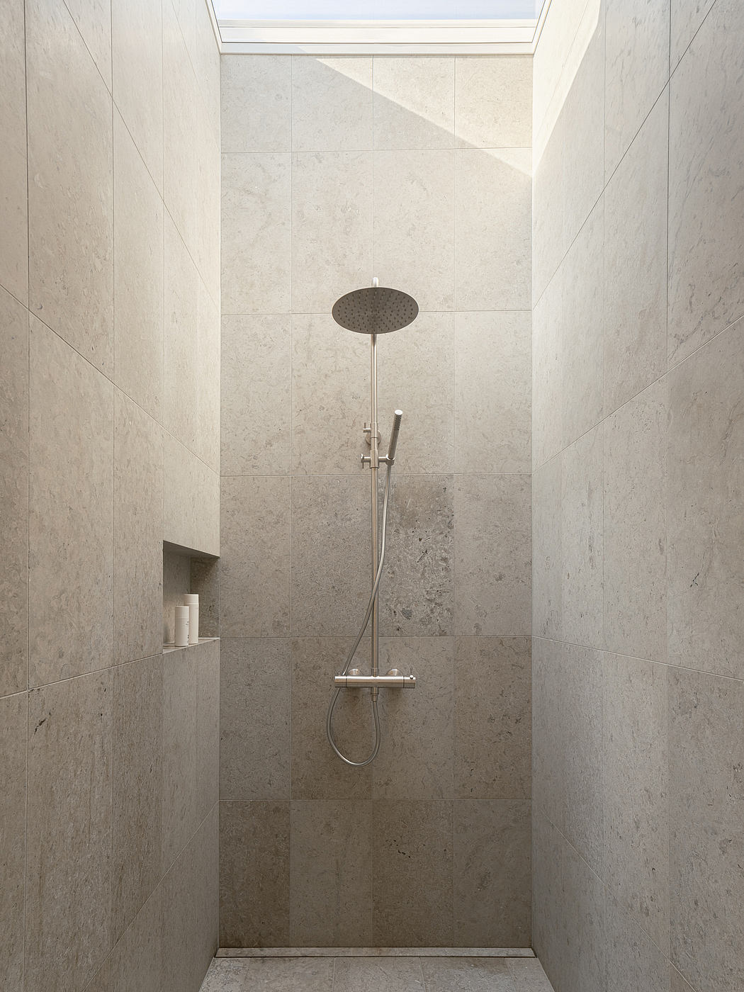 Sleek, minimalist shower enclosure with a large overhead showerhead and a recessed shelf.