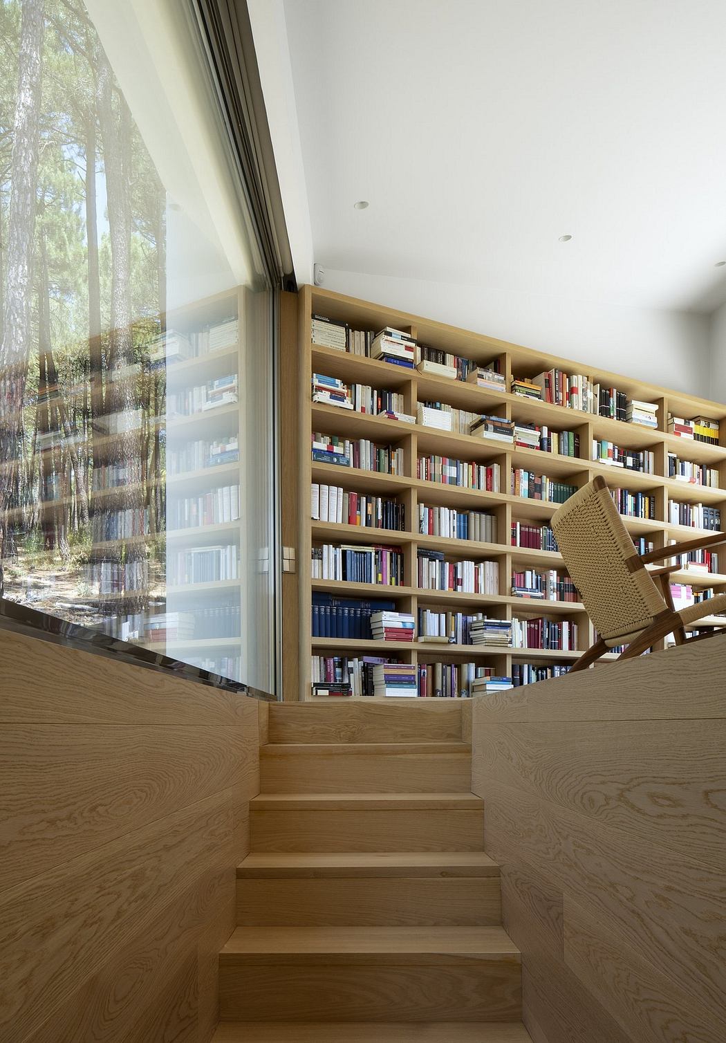 A cozy reading nook with floor-to-ceiling bookshelves and wooden steps leading up to a comfortable chair.