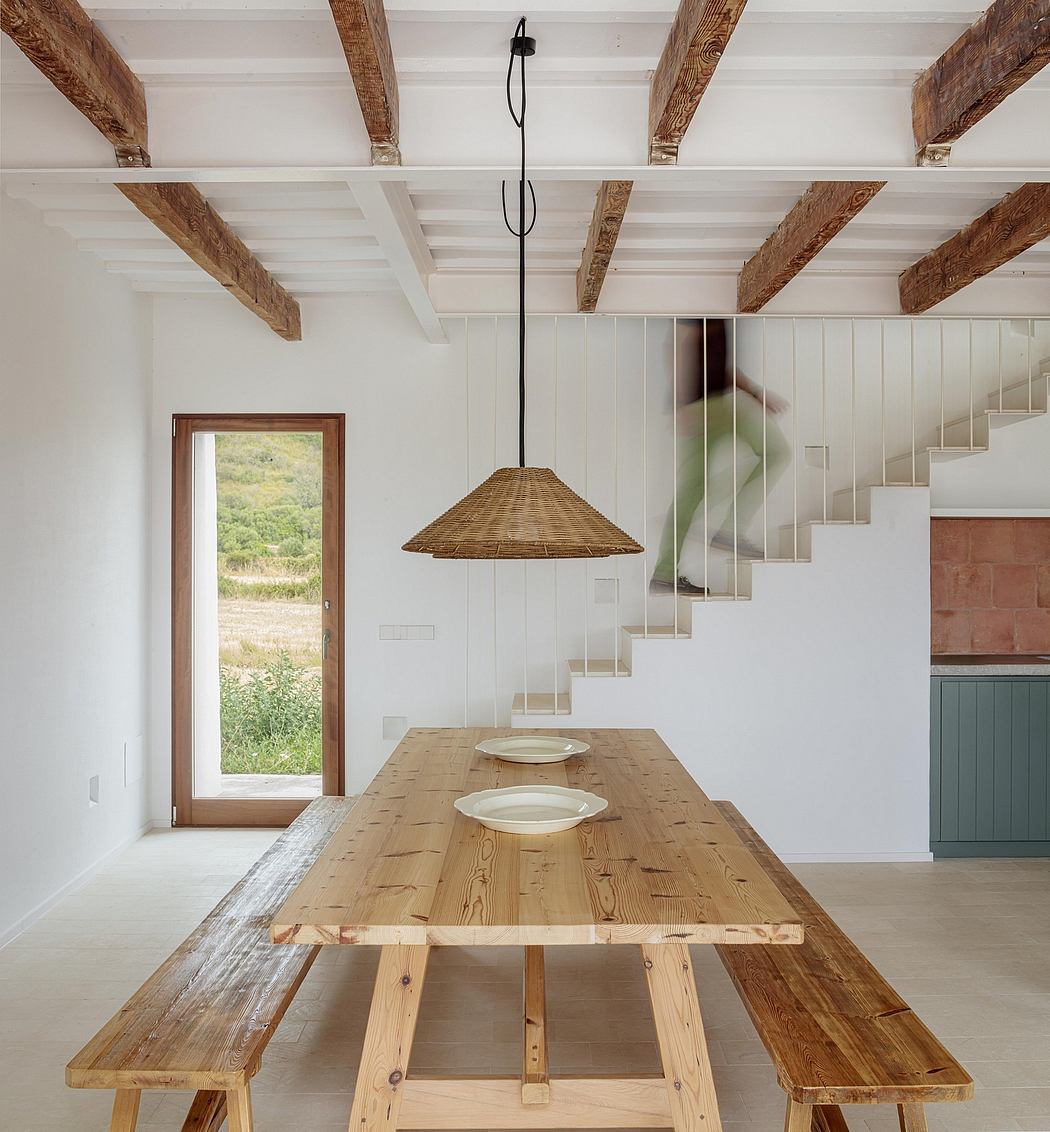Rustic dining room with exposed wooden beams, minimal furnishings, and woven pendant light.