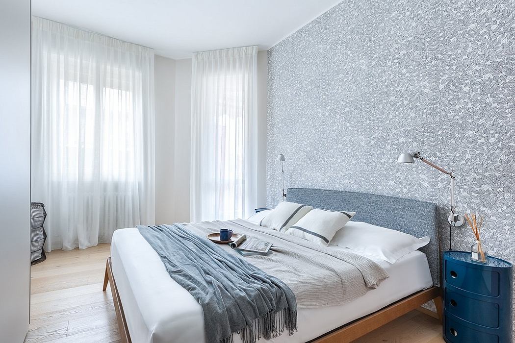 Minimalist bedroom with patterned wallpaper, white curtains, wood furniture, and blue accents.
