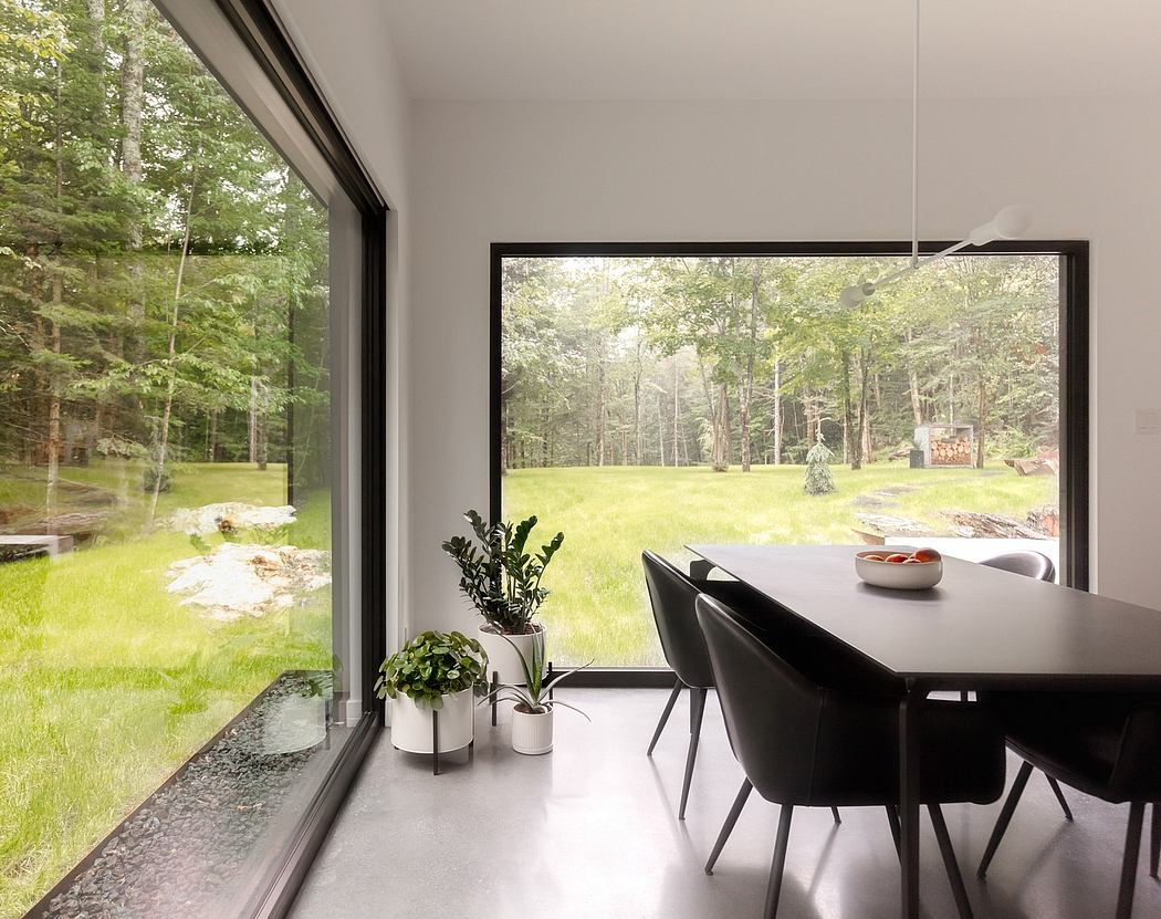 Modern dining room with floor-to-ceiling windows overlooking a lush, forested landscape.