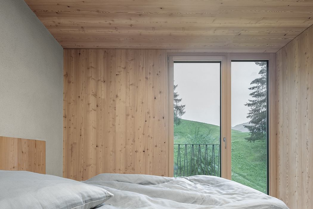 A minimalist bedroom with wooden walls, large window offering scenic mountain views.