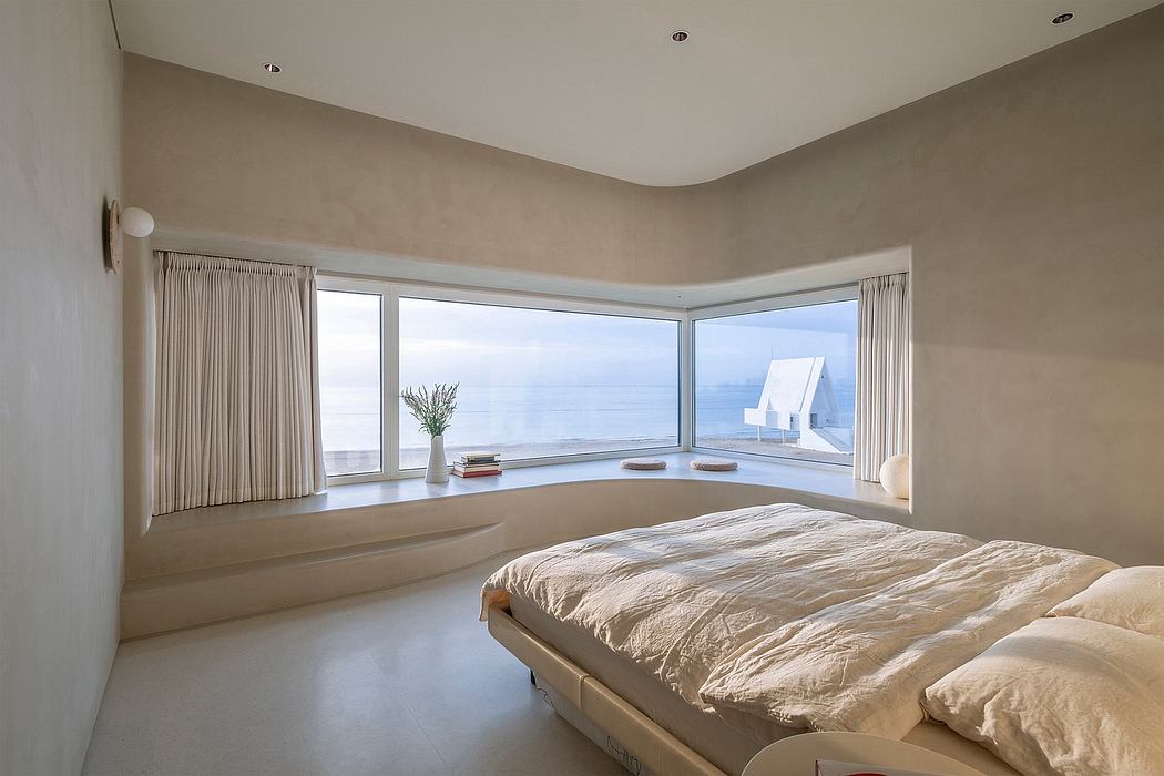 Spacious bedroom with large bay window overlooking the ocean, minimalist decor.