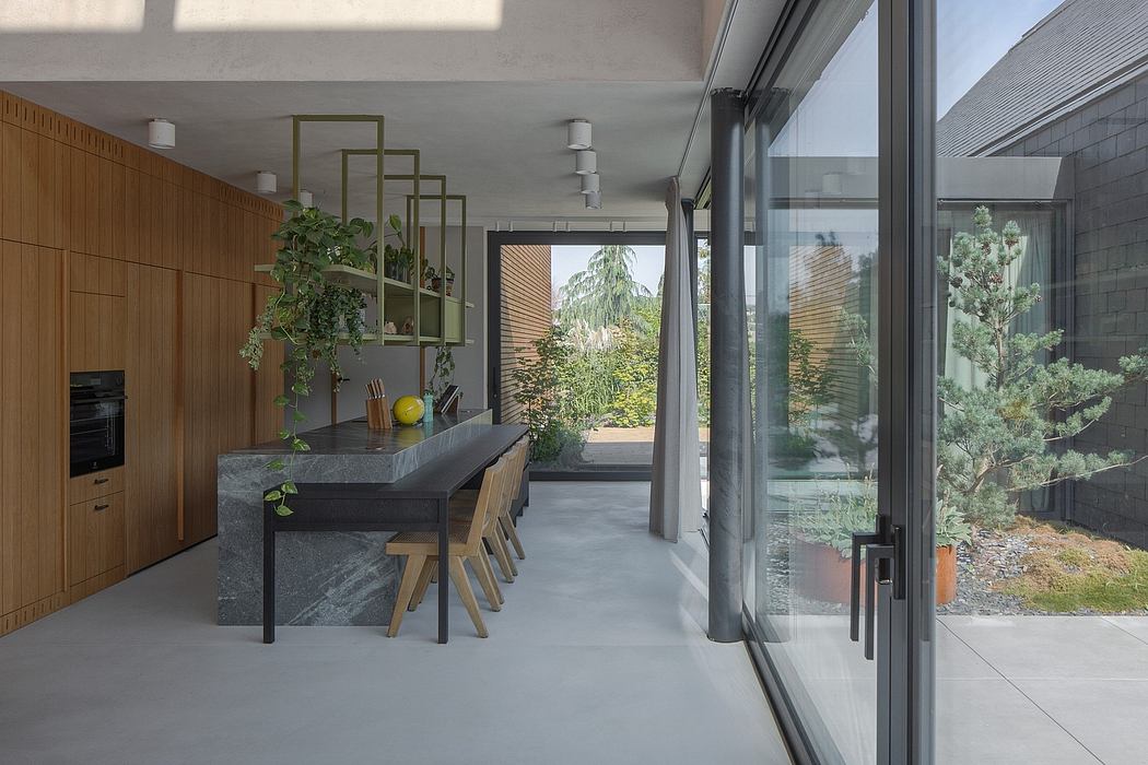 Sleek, modern kitchen with concrete countertop, wooden cabinetry, and floor-to-ceiling windows overlooking lush greenery.