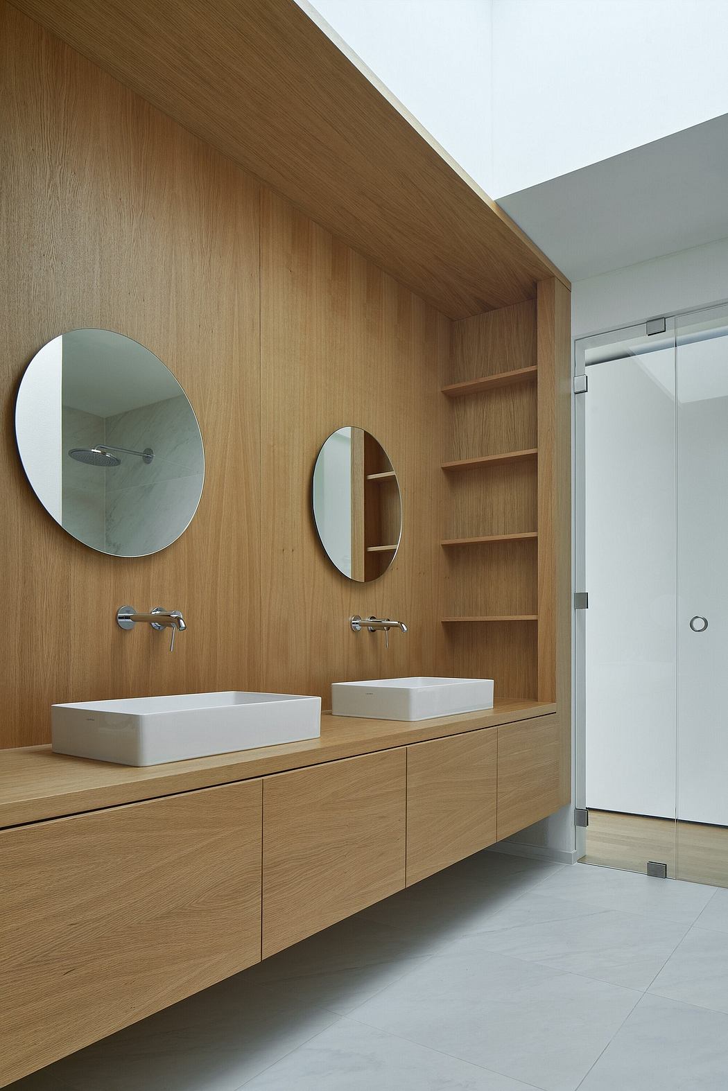 Modern bathroom with wooden vanity, two round mirrors, and built-in shelves.