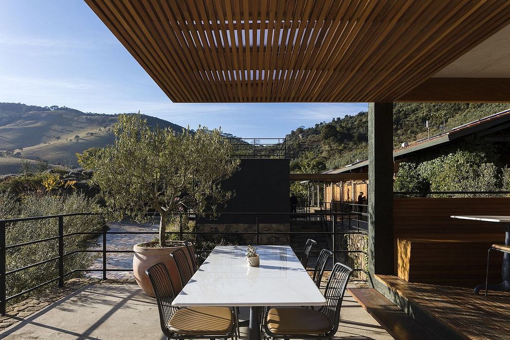 Wooden slat ceiling frames mountainous landscape, outdoor table with chairs on paved terrace.