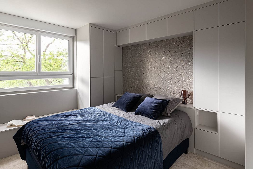 Minimalist bedroom design with gray built-in cabinets, dark bedding, and large window.