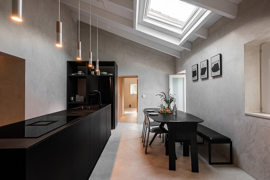 A modern, minimalist kitchen and dining area featuring sleek black cabinetry, pendant lights, and concrete walls.