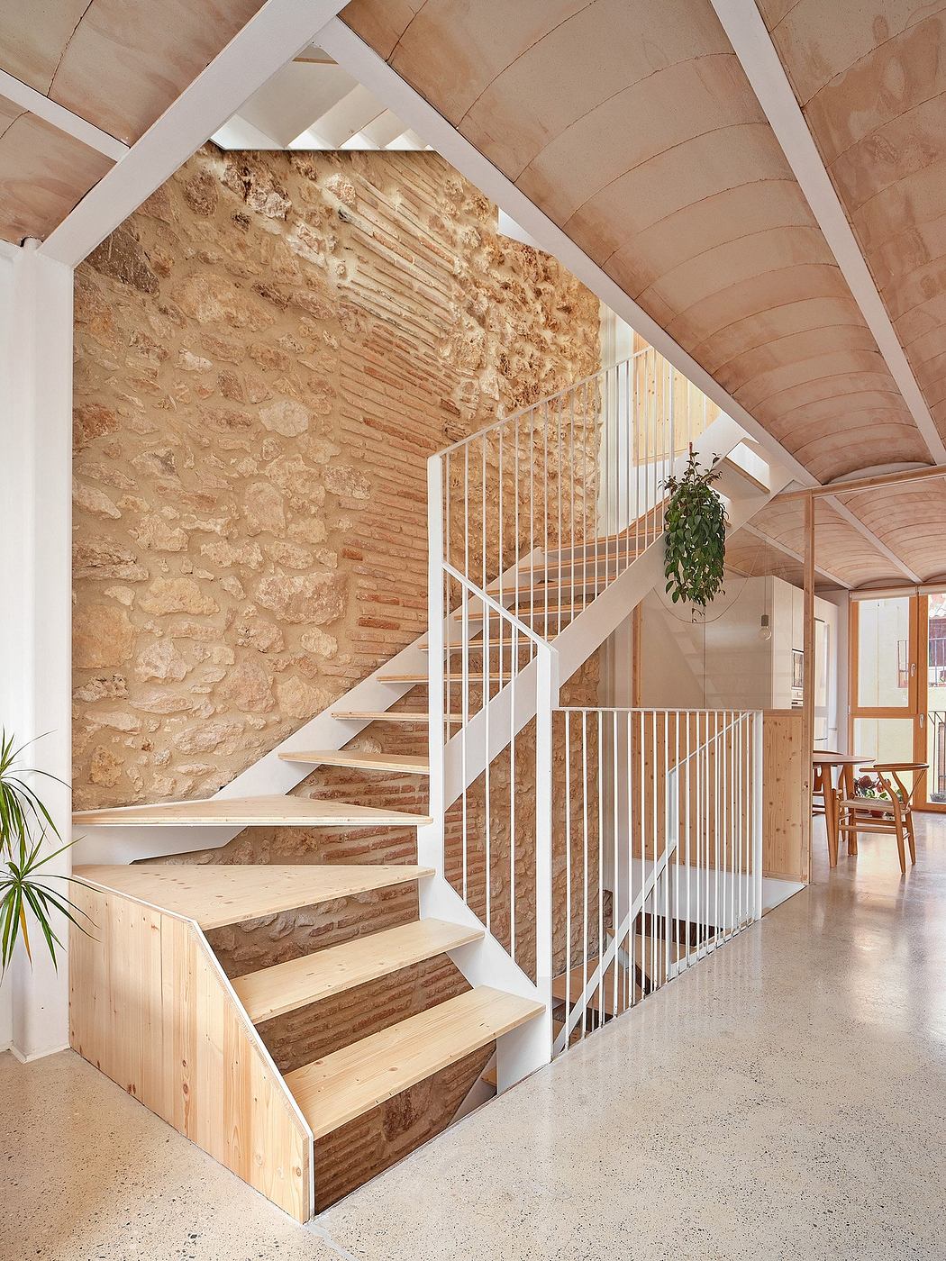 A warm, rustic staircase with exposed stone walls, wooden beams, and a decorative potted plant.