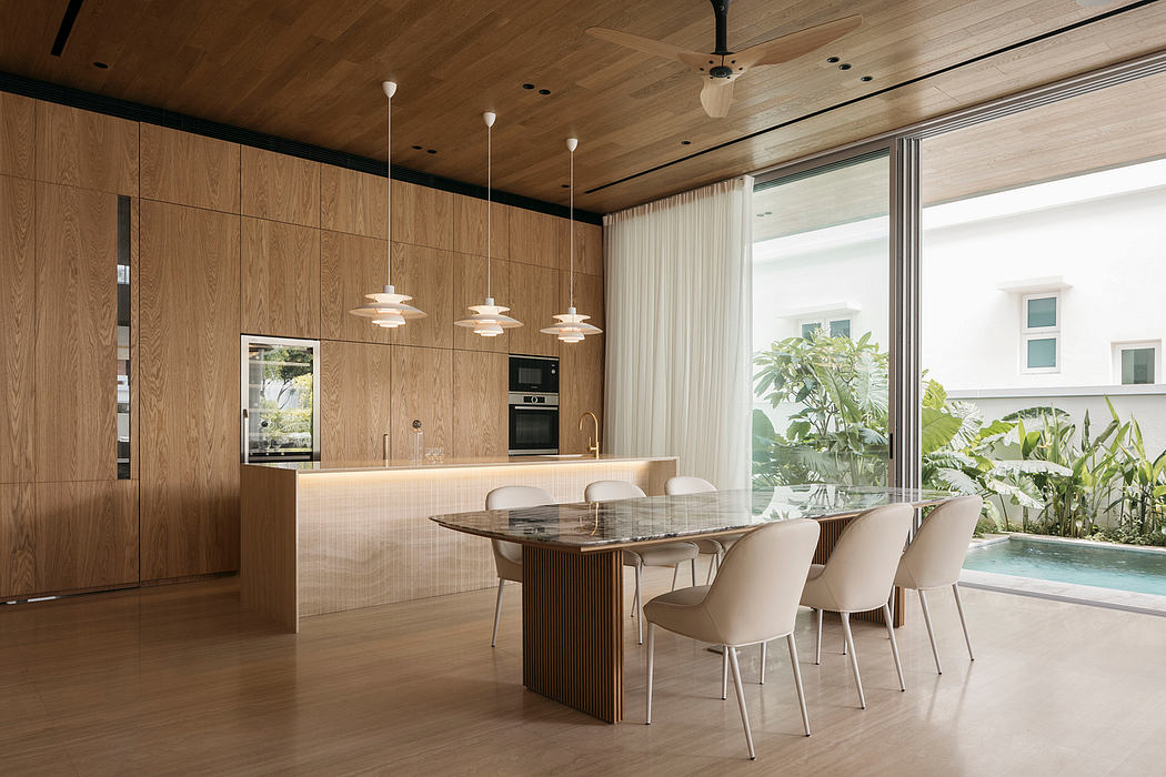 Sleek, modern kitchen and dining area with warm wood paneling, pendant lights, and outdoor view.