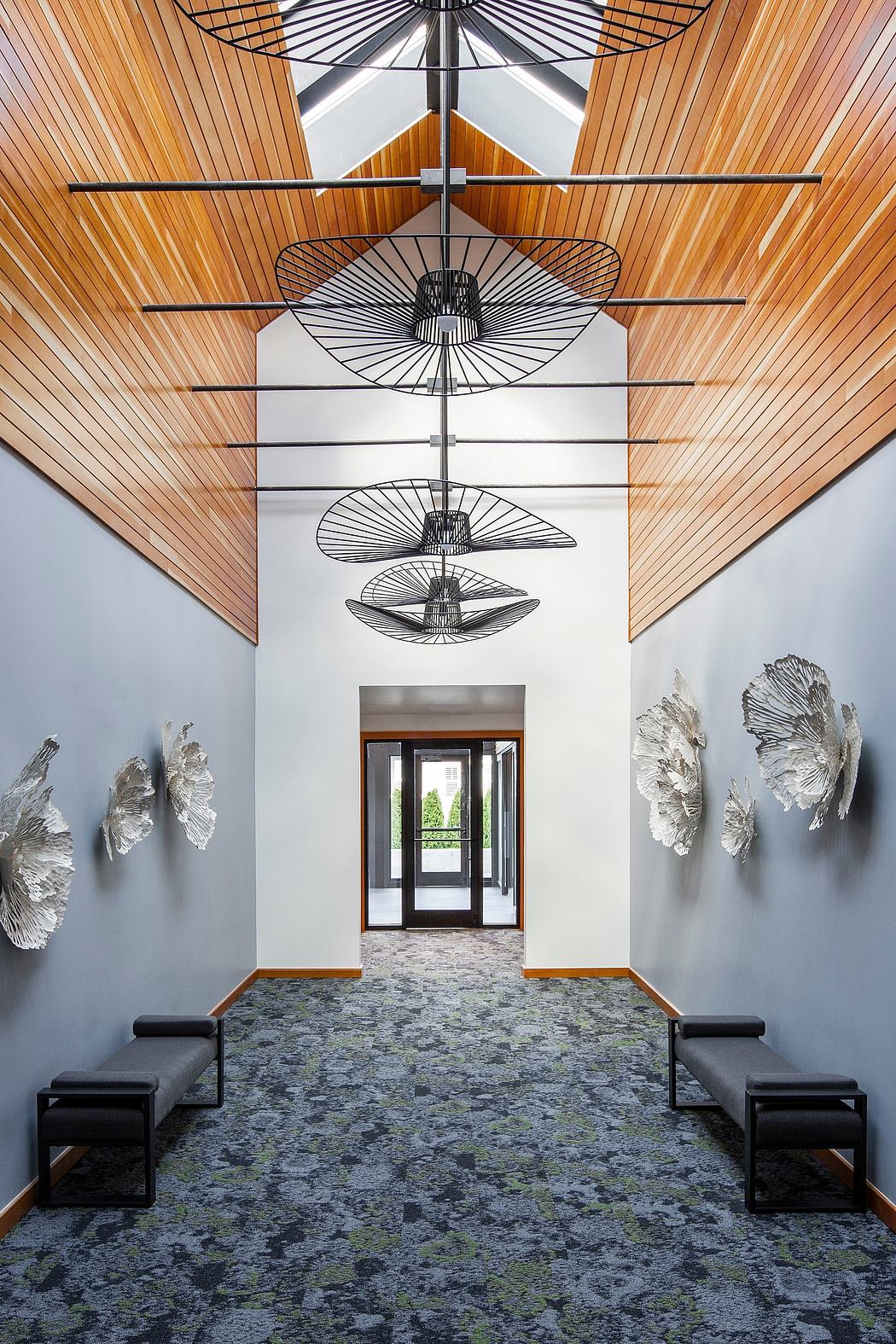 A grand entryway with a geometric lighting fixture, wooden slat ceiling, and abstract wall sculptures.