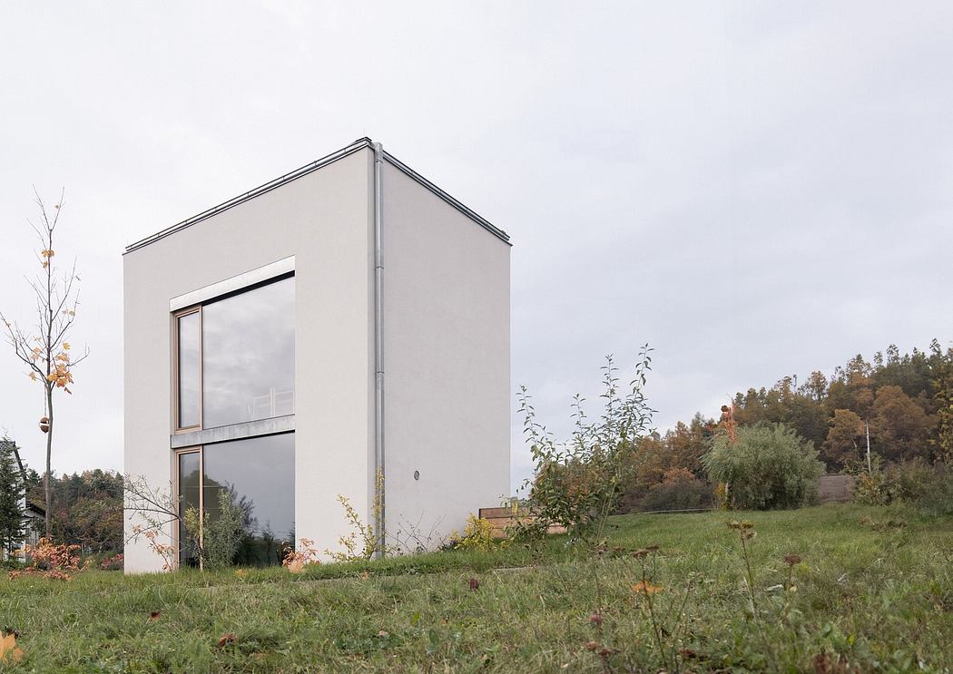 A modern, minimalist structure with glass panels overlooking a grassy, wooded landscape.
