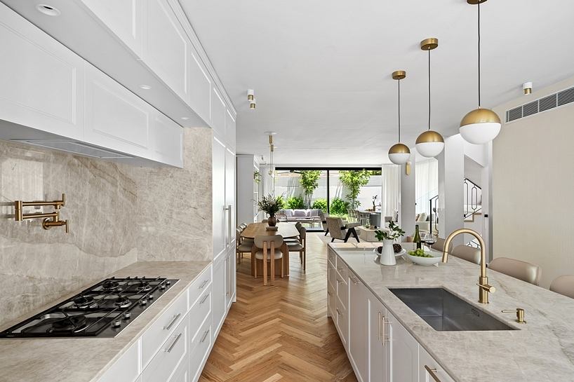 Chic, modern kitchen with sleek white cabinetry, gold light fixtures, and herringbone hardwood floors.