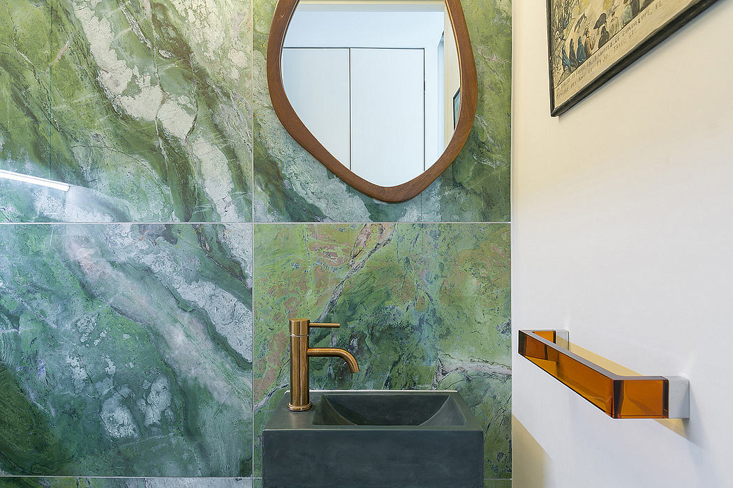 Elegant bathroom with striking green marble tiles, oval mirror, and sleek brass fixtures.