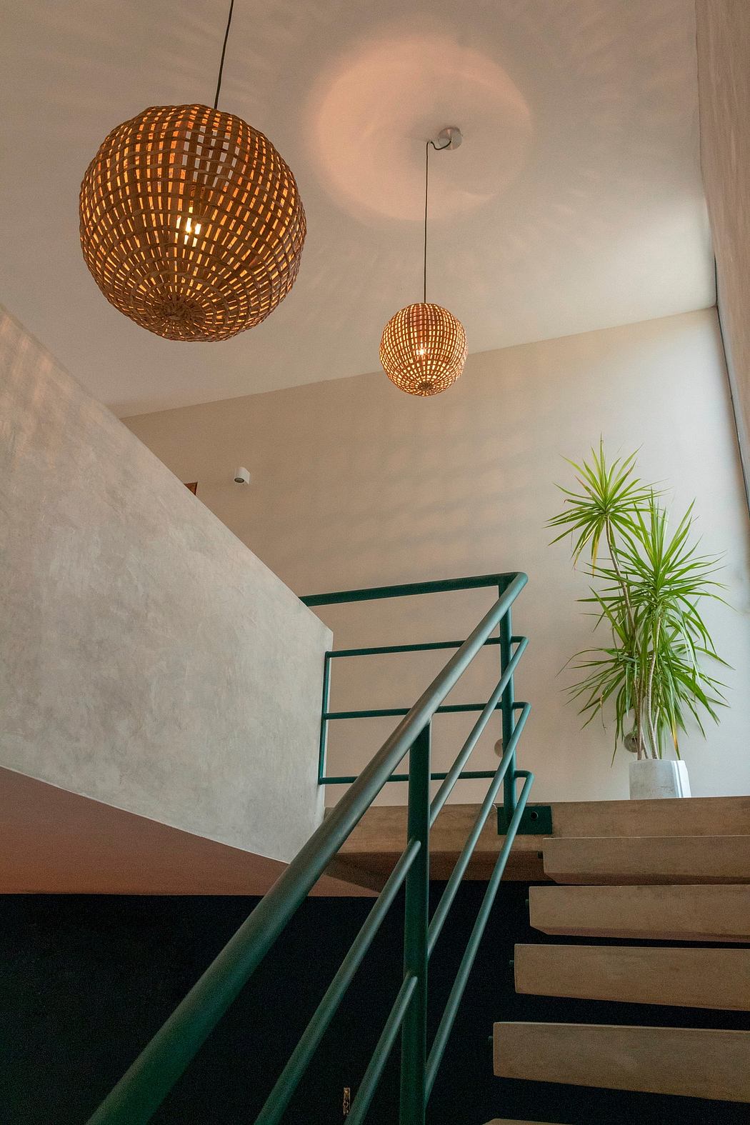 Warm pendant lighting, modern staircase, and tropical plant accent an interior space.