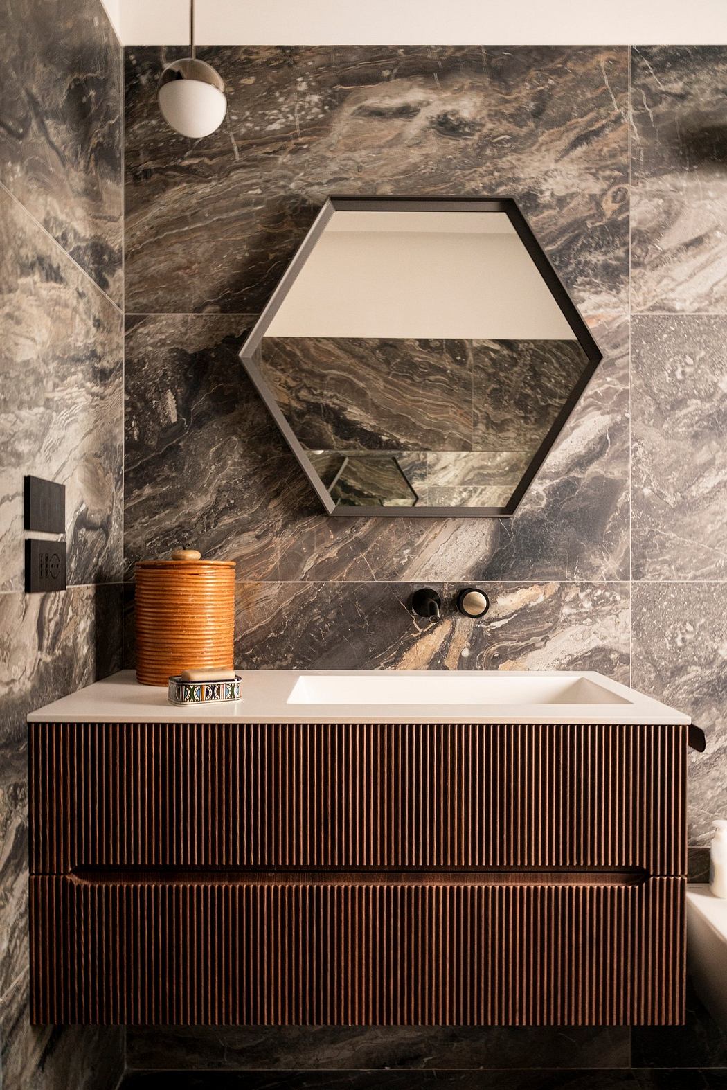Hexagonal mirror above a textured marble vanity with a wood-slatted cabinet below.