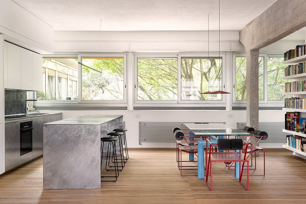 Minimalist modern kitchen and dining area with floor-to-ceiling windows overlooking trees.