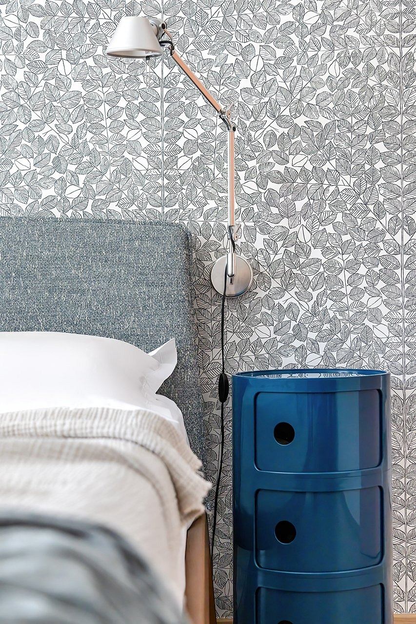 Monochrome leaf-patterned wallpaper, modern bedside lamp, and navy blue dresser in cozy bedroom.