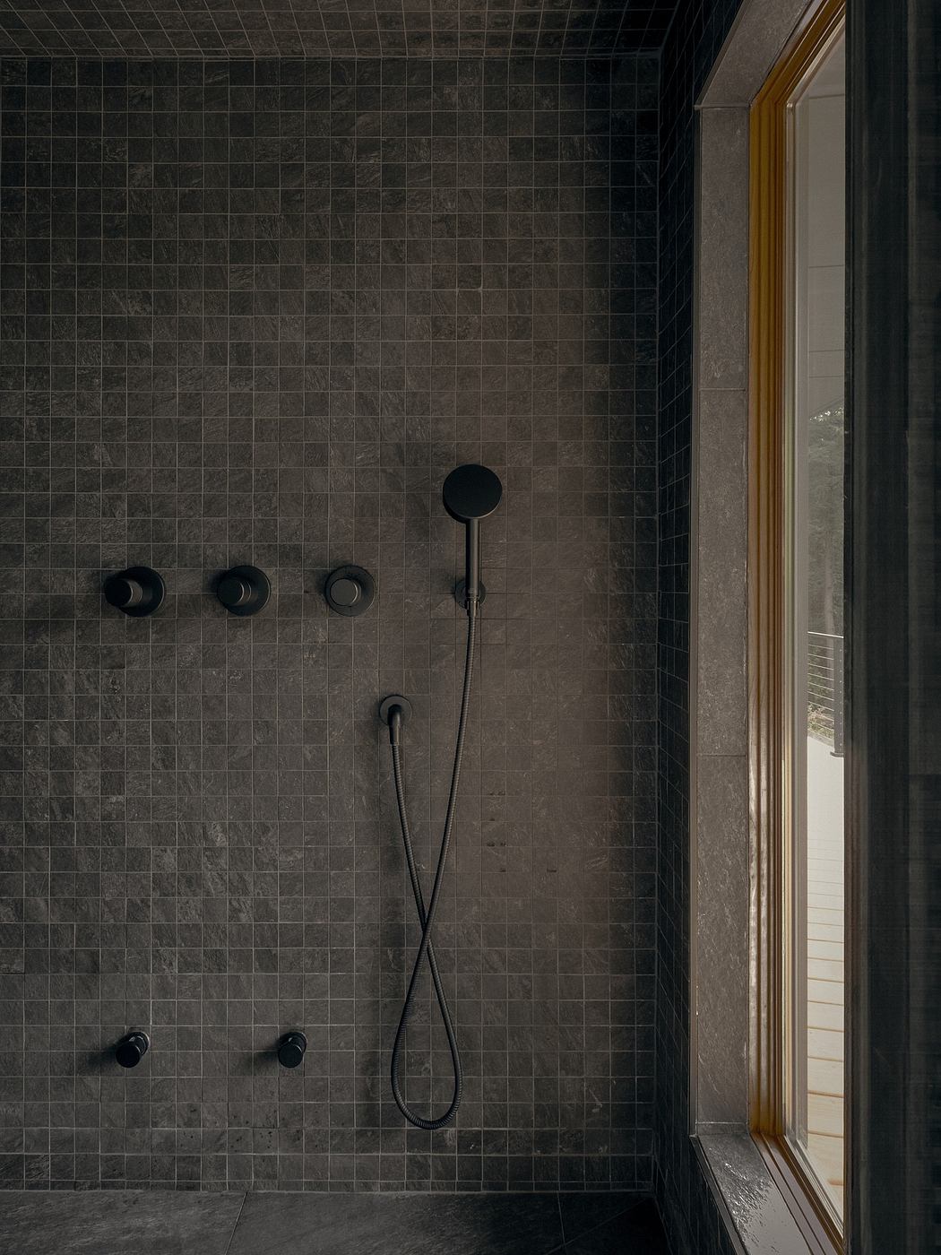 Sleek modern bathroom with dark tiled walls, recessed fixtures, and a large window.