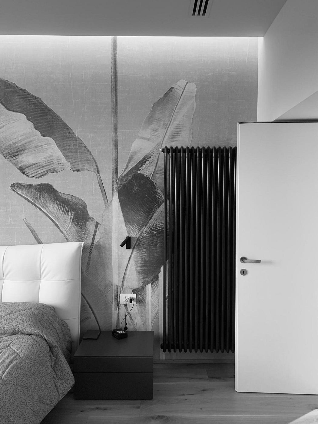 A cozy bedroom with large banana leaves on the wall, a radiator, and a minimalist nightstand.