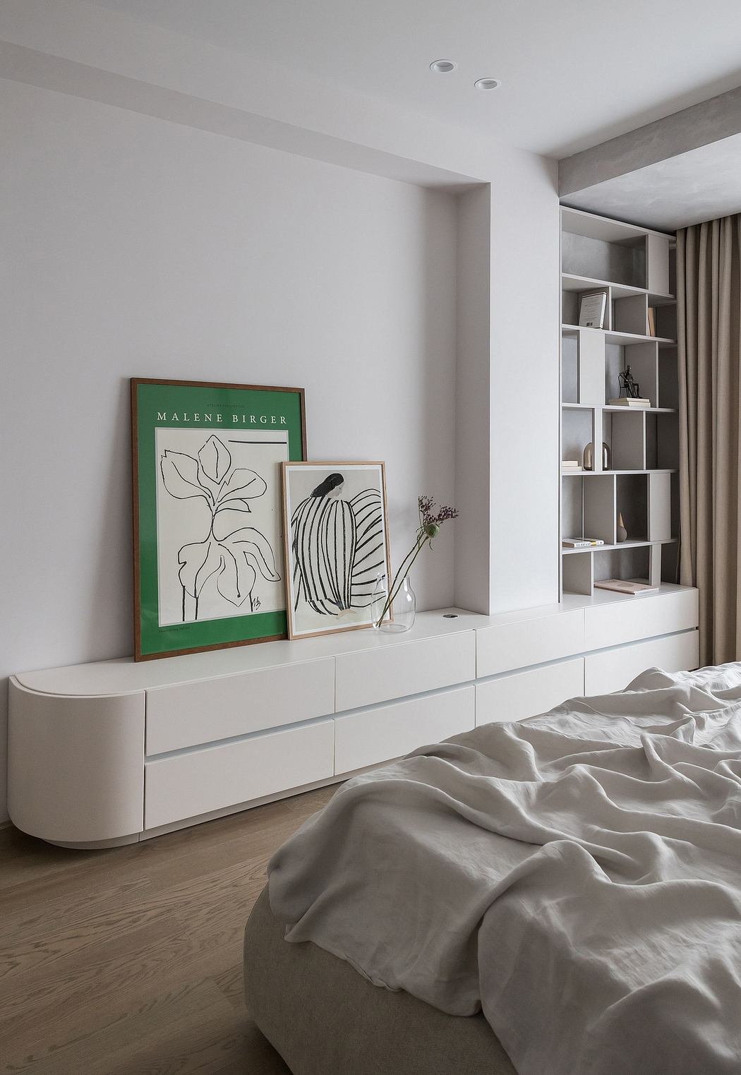 Minimalist bedroom with monochrome artwork, sleek white furnishings, and built-in shelving.