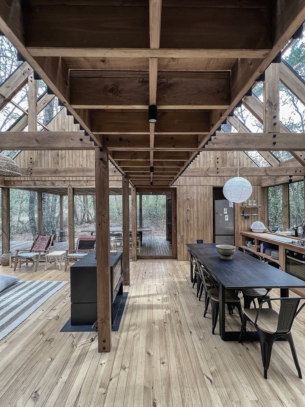 A rustic, open-concept interior with wooden beams, large windows, and a dining area.